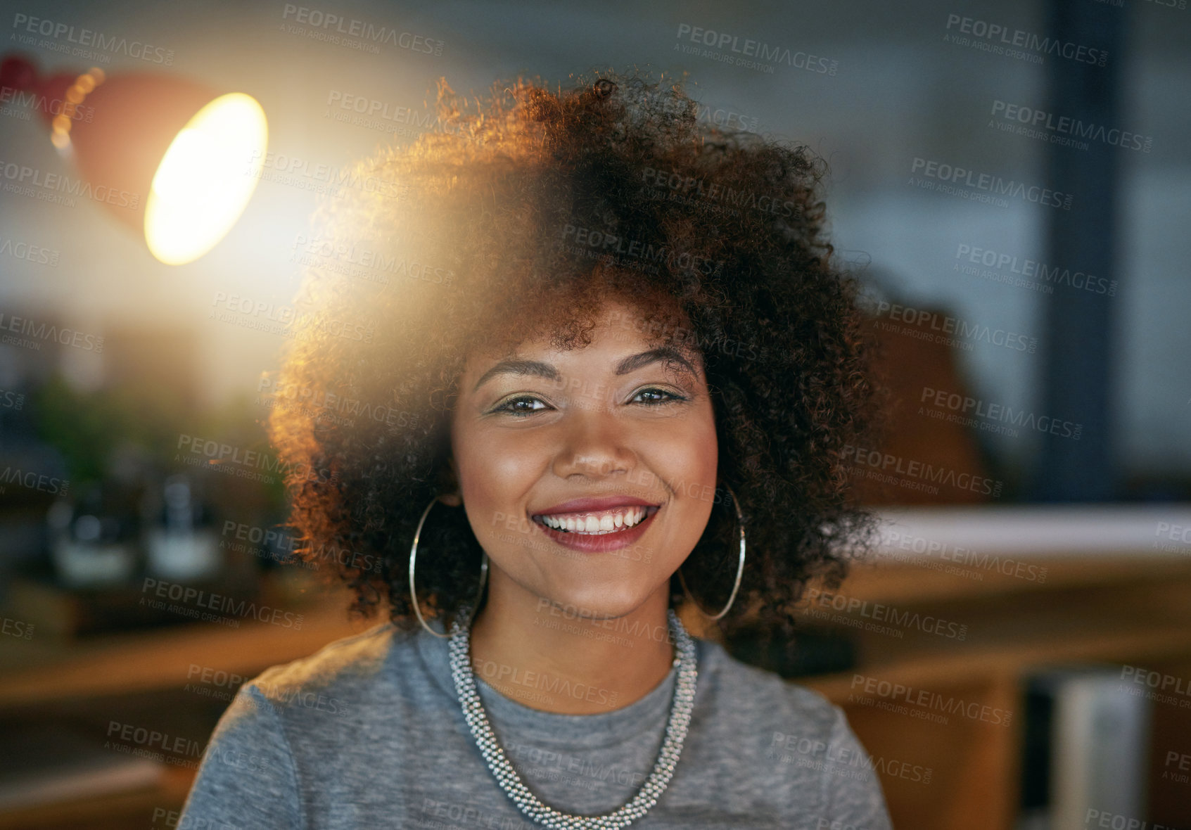 Buy stock photo Lamp, portrait and woman in office at night, working at desk for business deadline. Afro, face and smile of confident or happy African design person in creative workplace for late evening project