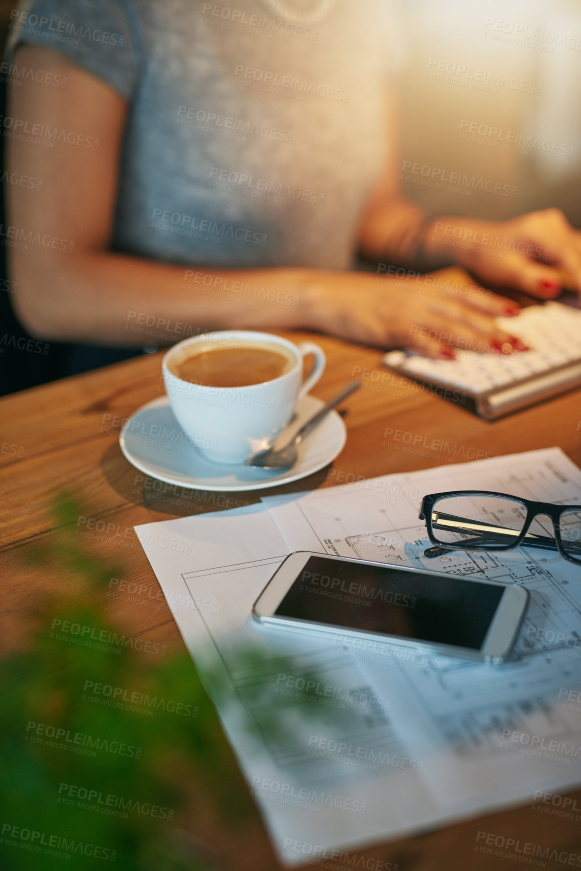 Buy stock photo Cropped shot of a woman working on a computer with coffee, a phone and paperwork in the foreground