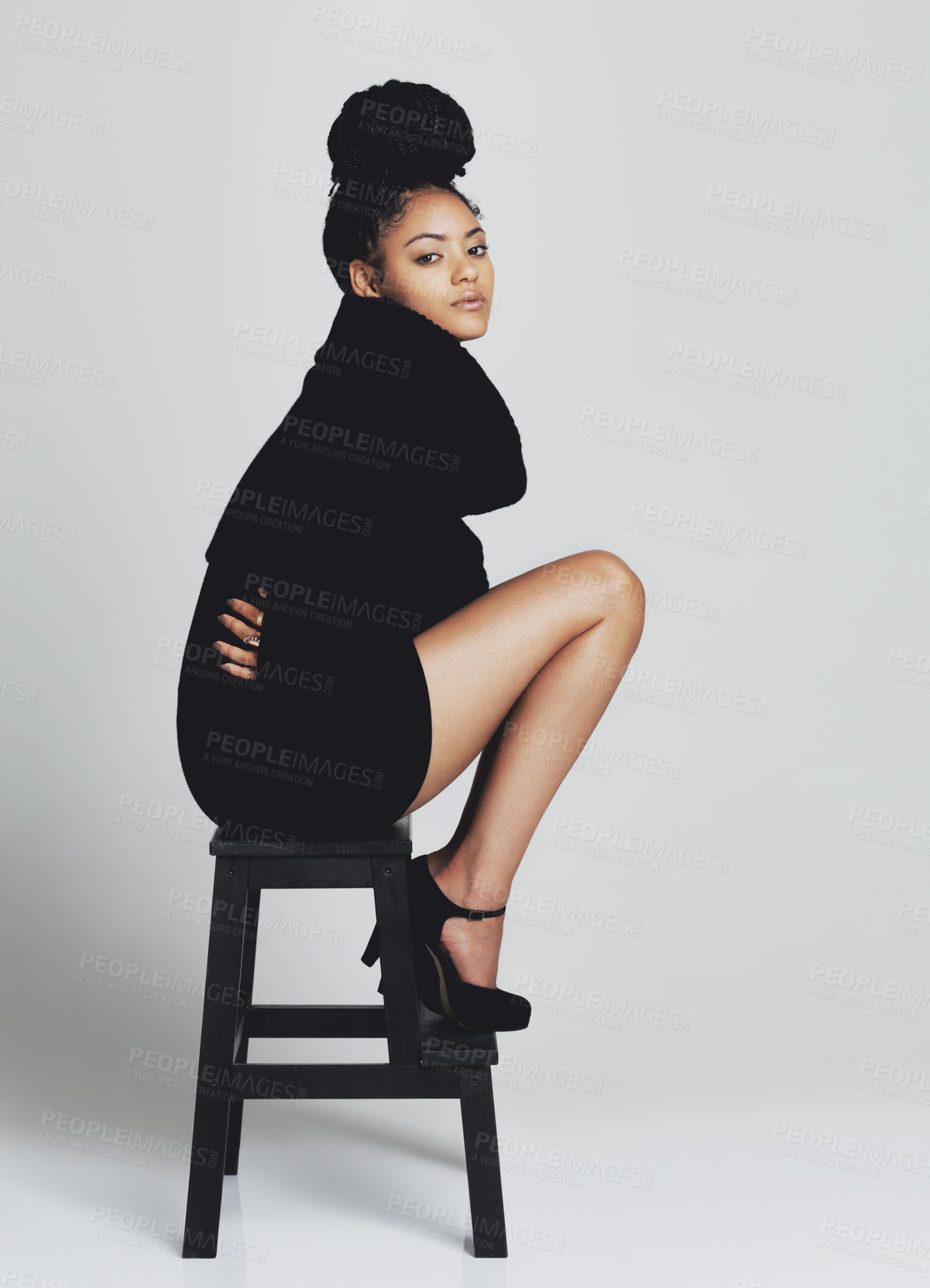 Buy stock photo Studio shot of a fashionable young woman posing on a stool in a black dress