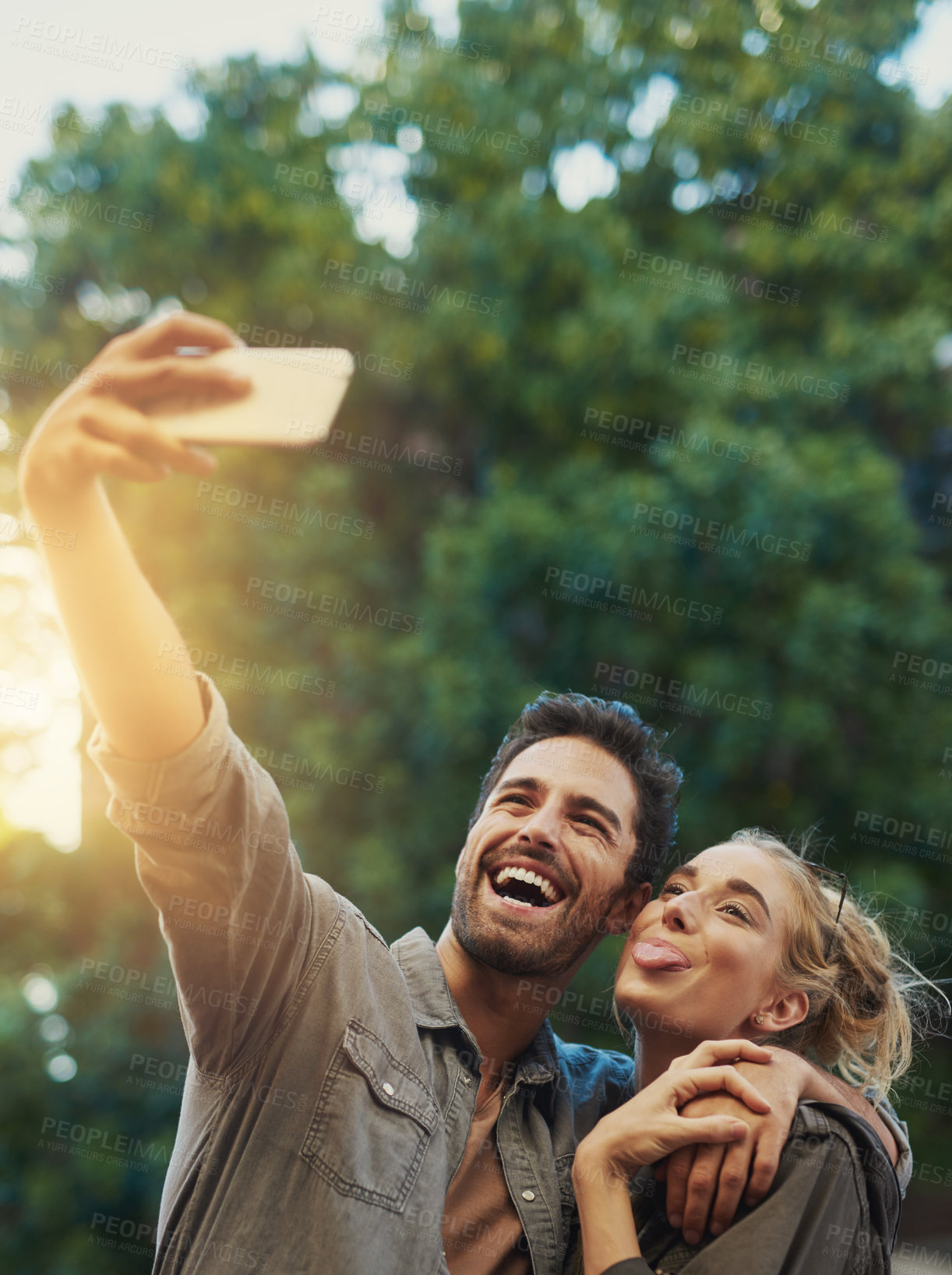 Buy stock photo Couple, selfie and hug with smile in park, tongue and care with connection, love and photography. People, man and woman with trees, profile picture and funny with memory on social network in Berlin