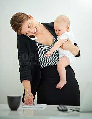 Buy stock photo Shot of a successful young businesswoman carrying her adorable baby boy while talking on the phone