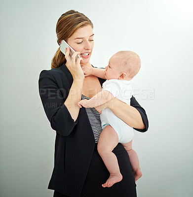 Buy stock photo Shot of a successful young businesswoman carrying her adorable baby boy while talking on the phone