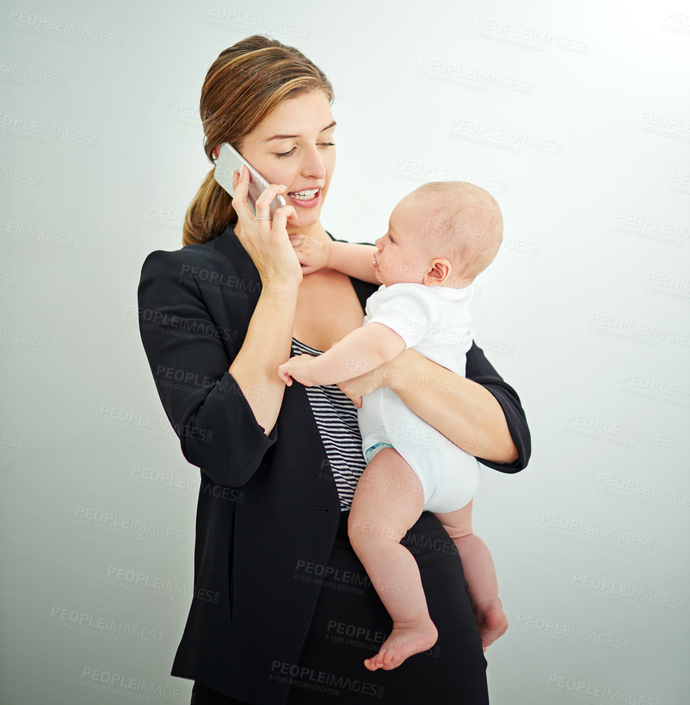 Buy stock photo Shot of a successful young businesswoman carrying her adorable baby boy while talking on the phone