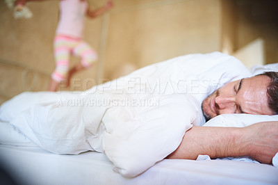 Buy stock photo Shot of a sleeping dad with his little daughter jumping on the end of the bed