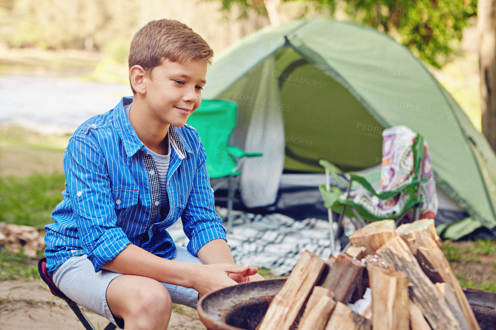 Buy stock photo Shot of a young boy sitting by an unlit campfire