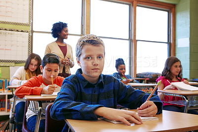 Buy stock photo Shot of a young boy sitting in class with his teacher and classmates blurred in the background