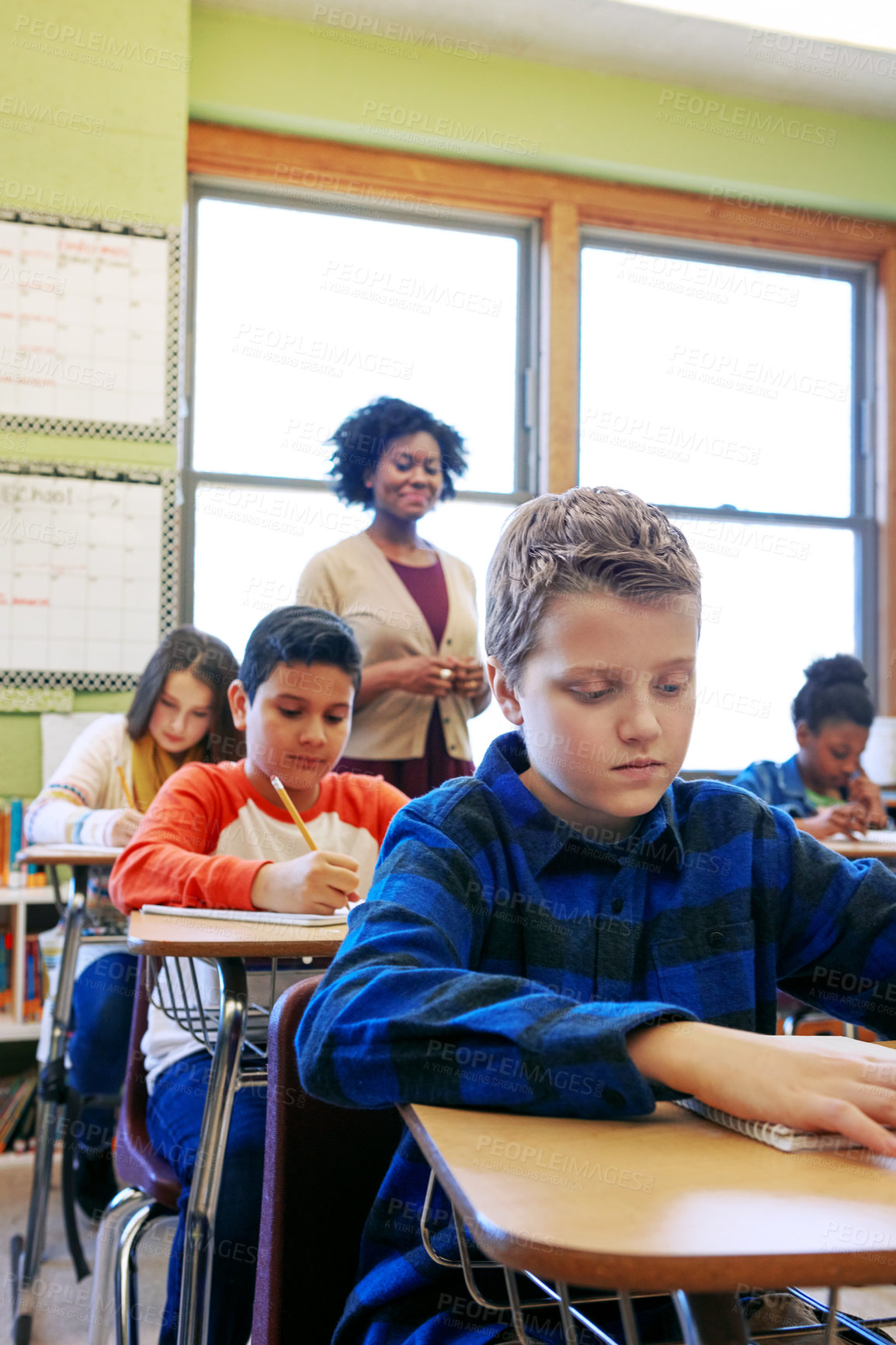 Buy stock photo Shot of a young boy sitting in class with his teacher and classmates blurred in the background