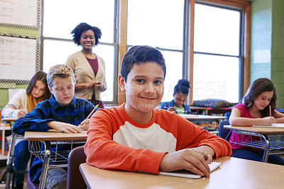 Buy stock photo Shot of a young boy sitting in class with his teacher and classmates blurred in the background