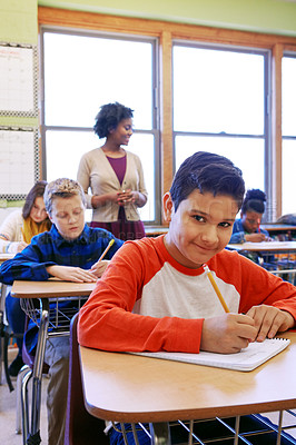 Buy stock photo Shot of a young boy sitting in class with his teacher and classmates blurred in the background