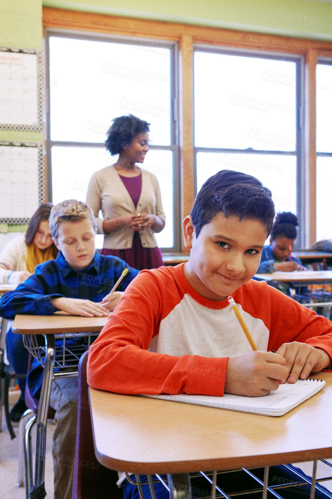 Buy stock photo Shot of a young boy sitting in class with his teacher and classmates blurred in the background