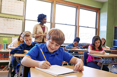 Buy stock photo Shot of a young boy sitting in class with his teacher and classmates blurred in the background