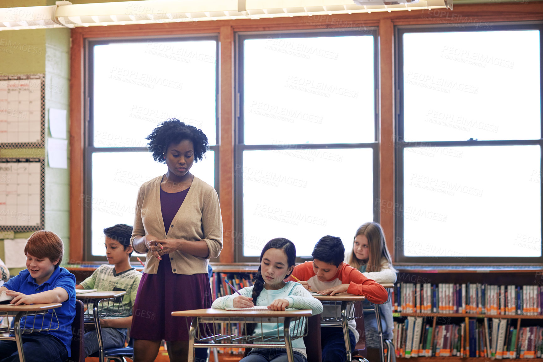 Buy stock photo Shot of a group of elementary children writing a test while a teacher observes