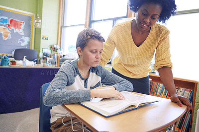 Buy stock photo A young teacher assisting a student with classwork at his desk