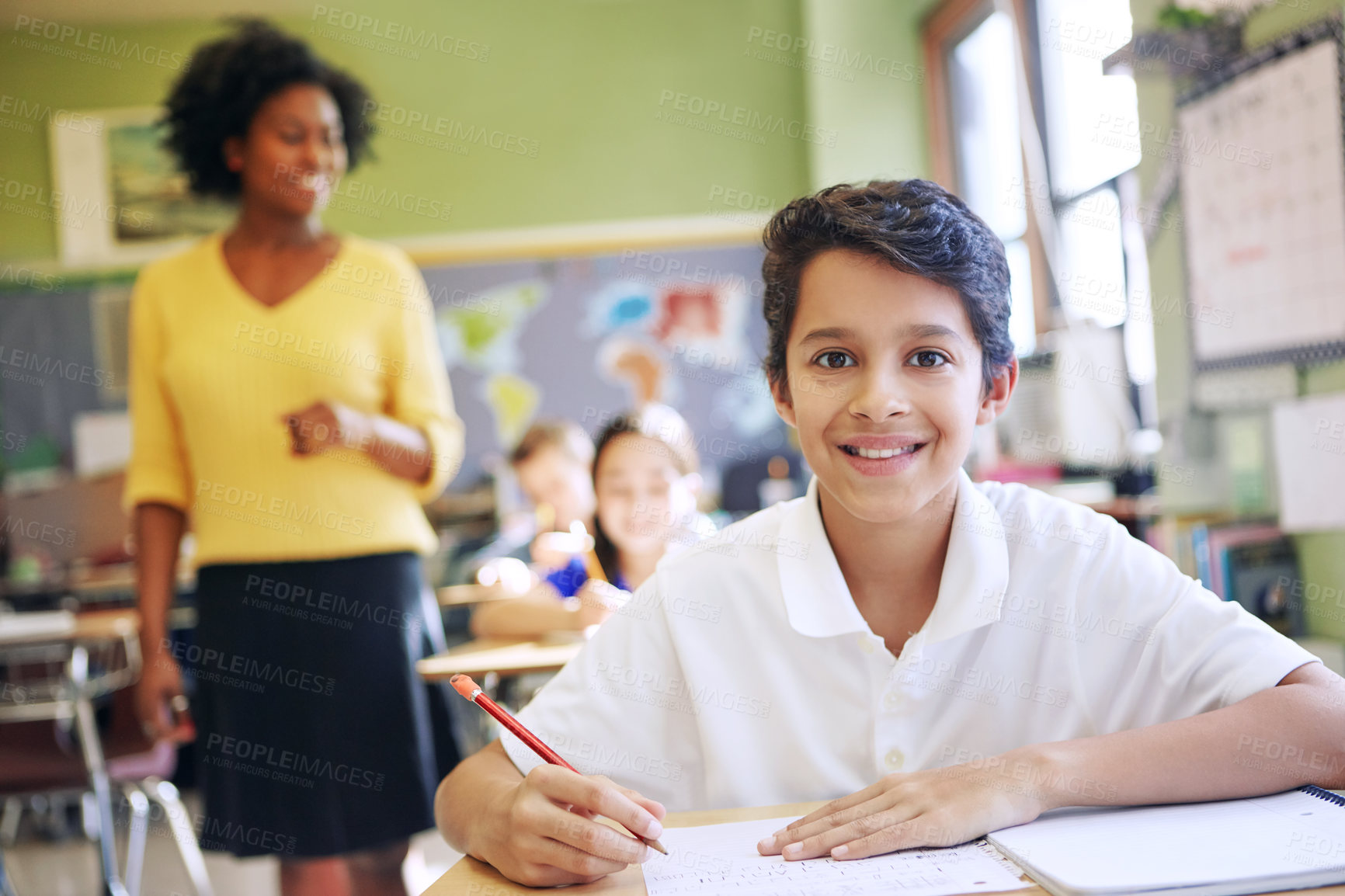 Buy stock photo Shot of a young boy sitting in class with his teacher and classmates blurred in the background