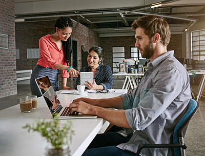 Buy stock photo Shot of a young man working on a laptop with his colleagues in the background