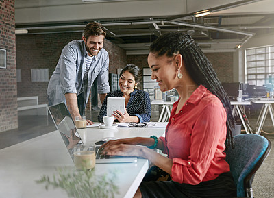 Buy stock photo Shot of a young woman working on a laptop with her colleagues in the background