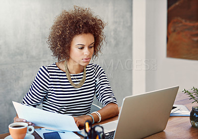 Buy stock photo Shot of a young woman working on a laptop and reading paperwork at home