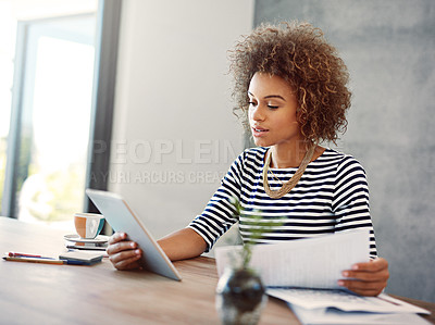 Buy stock photo Shot of a young woman a digital tablet and reading paperwork while working at home