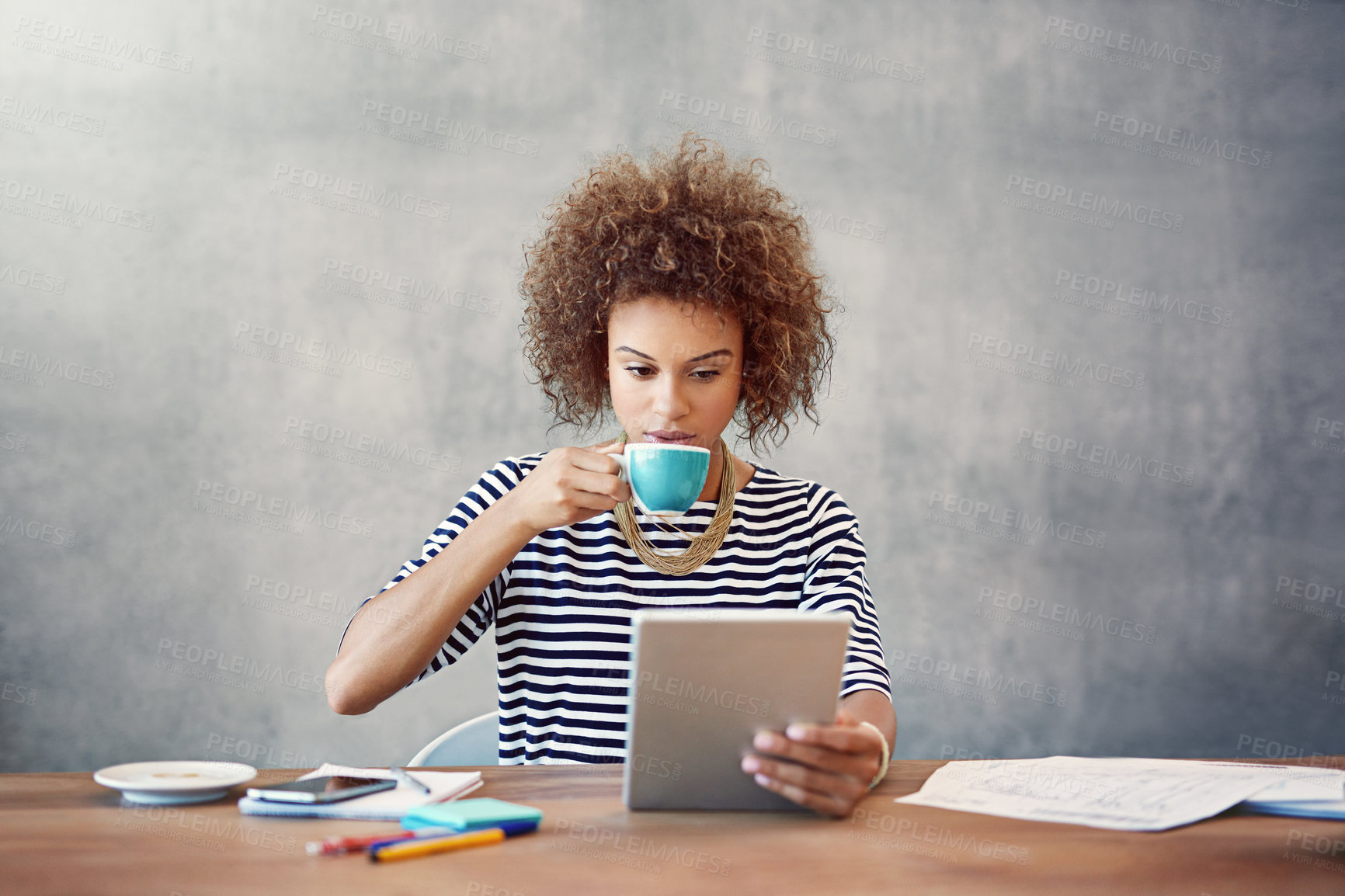 Buy stock photo Shot of a young woman drinking a coffee while working at home with a digital tablet