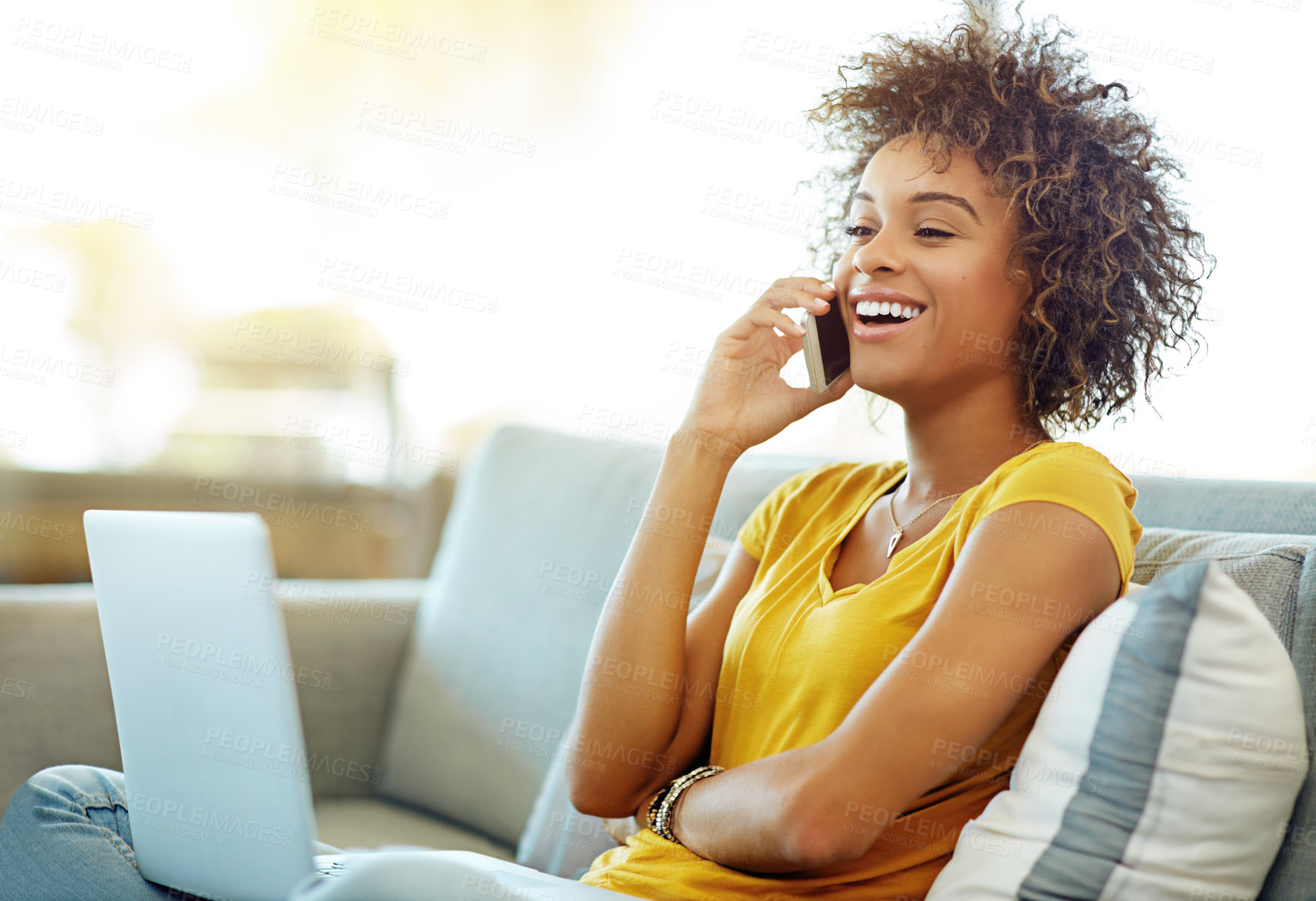 Buy stock photo Shot of a young woman talking on her phone while using a laptop on a relaxing day at home