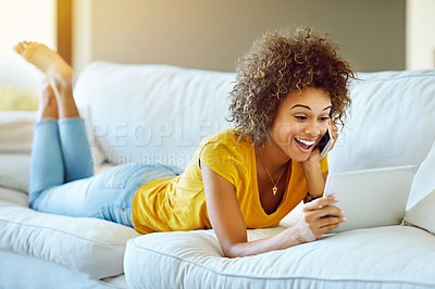 Buy stock photo Shot of a young woman talking on her phone while using a digital tablet on a relaxing day at home