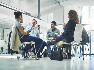 Buy stock photo Group of talking business professionals sitting together in a circle for a team meeting. A bunch of design employees and senior leader working, having a strategy and planning session in modern office