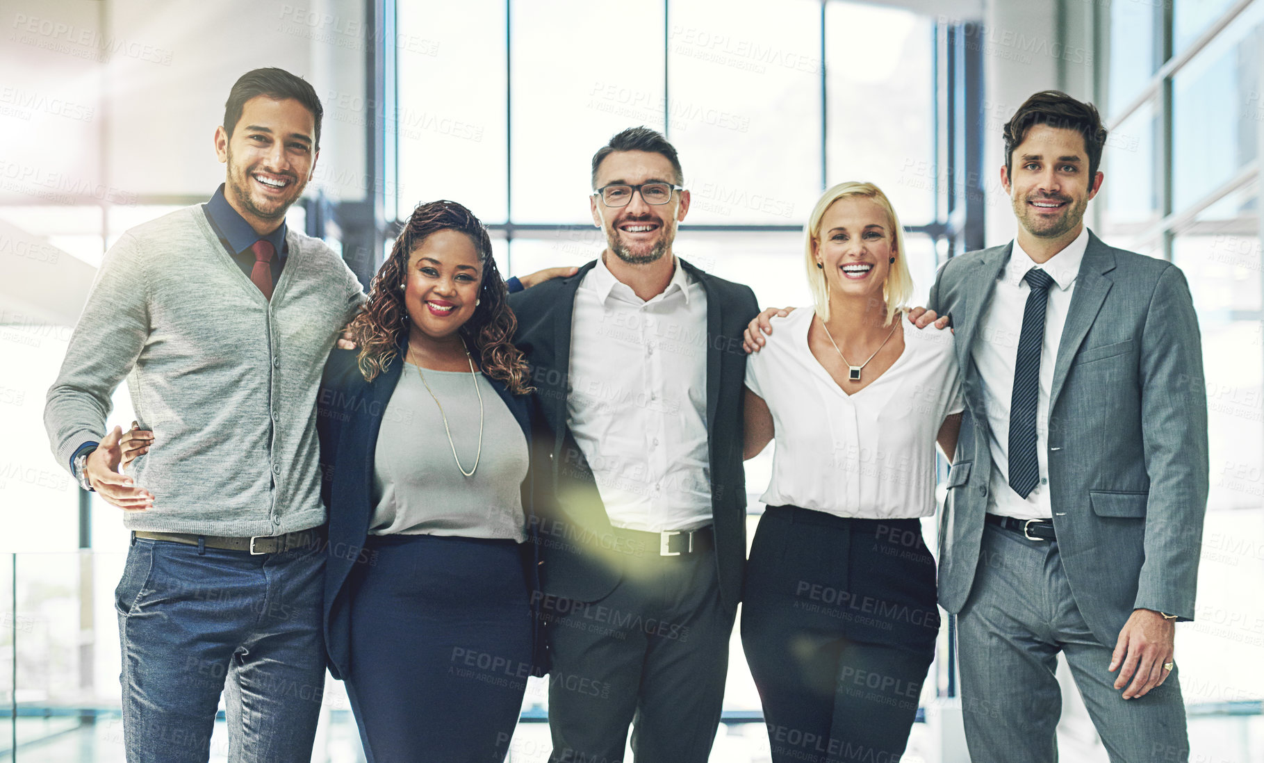 Buy stock photo Portrait of a diverse group of smiling coworkers standing arm in arm in an office