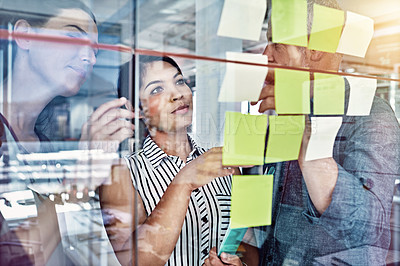 Buy stock photo Cropped shot of three colleagues looking at sticky notes on a glass board