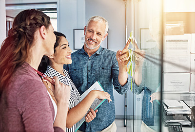 Buy stock photo Cropped shot of three colleagues looking at sticky notes on a glass board