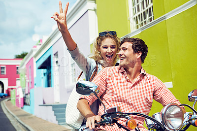 Buy stock photo Shot of a young couple riding a scooter through colorful city streets