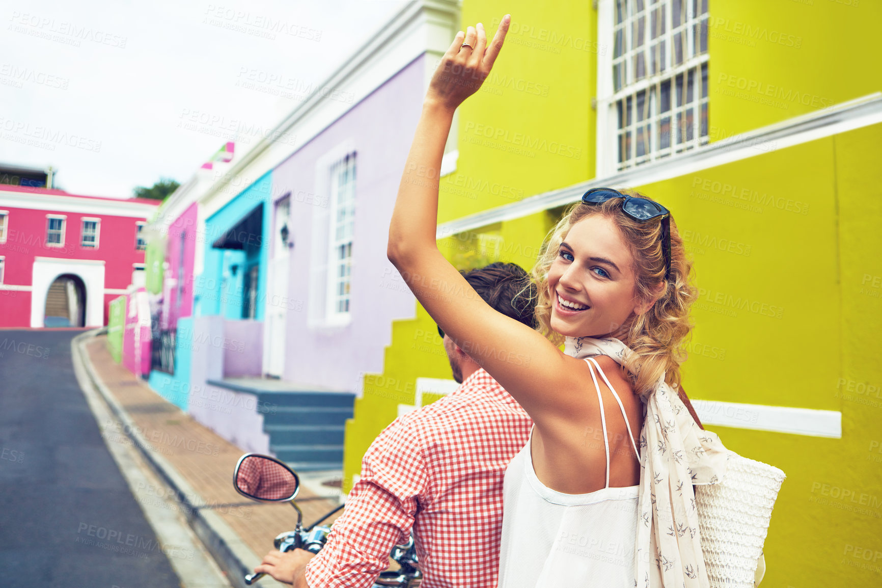 Buy stock photo Shot of a young couple riding a scooter through colorful city streets