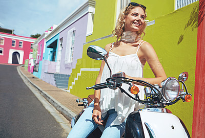 Buy stock photo Shot of a young woman riding a scooter through colorful city streets