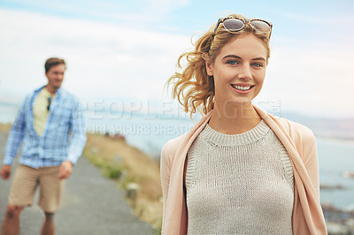 Buy stock photo Shot of a young woman walking outdoors with her boyfriend blurred in the background