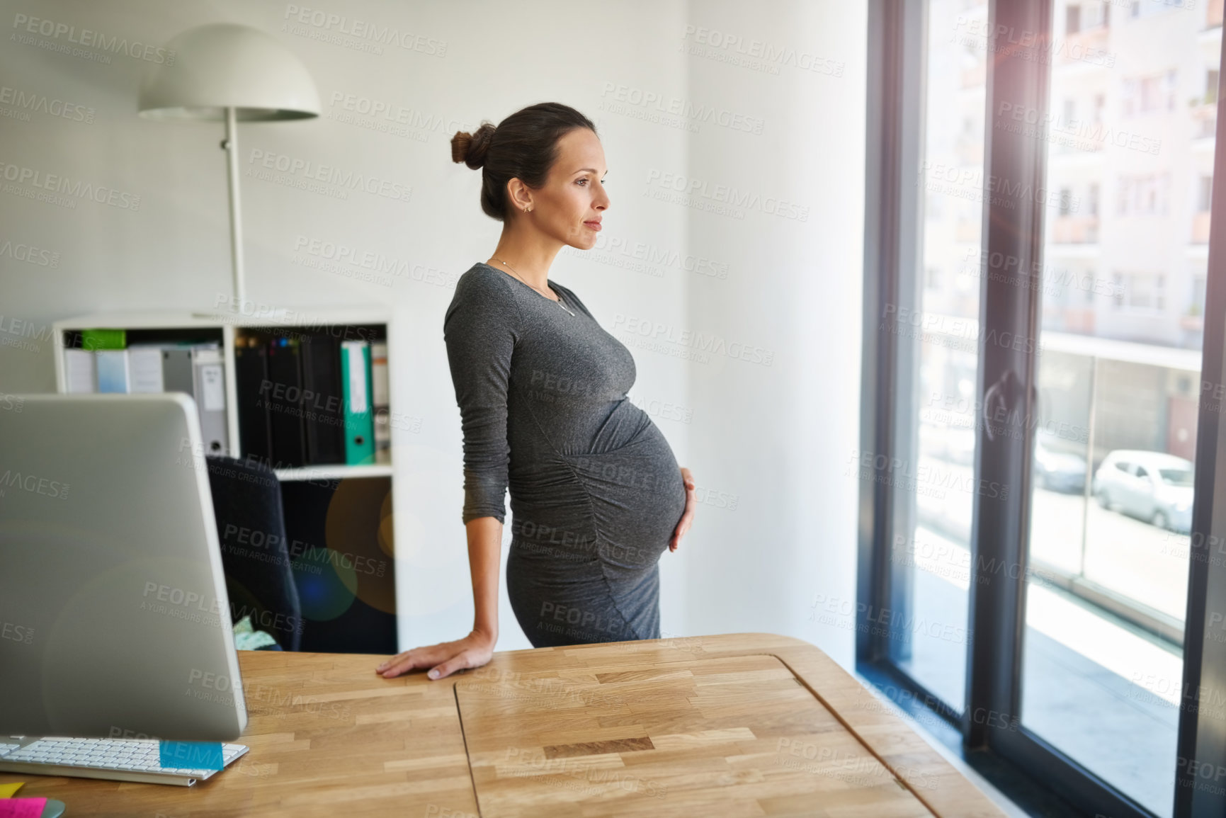 Buy stock photo Shot of a pregnant businesswoman standing in her office holding her stomach