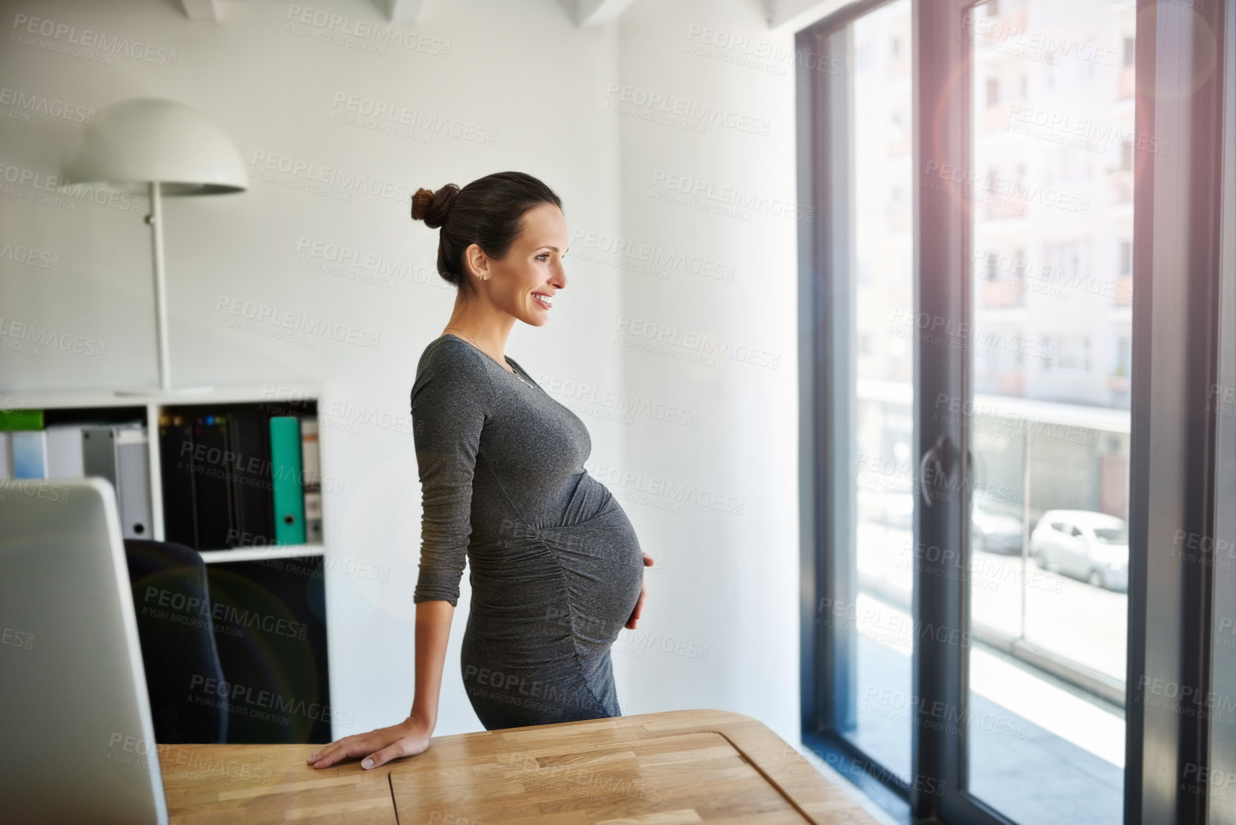 Buy stock photo Shot of a pregnant businesswoman standing in her office holding her stomach