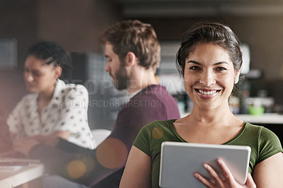Buy stock photo Portrait of a young woman using a digital tablet in a modern office with her colleagues in the background