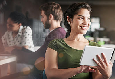 Buy stock photo Shot of a young woman using a digital tablet in a modern office with her colleagues in the background