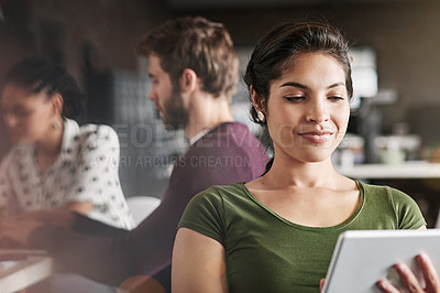 Buy stock photo Shot of a young woman using a digital tablet in a modern office with her colleagues in the background