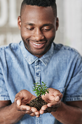 Buy stock photo Shot of a young man holding a plant growing out of soil in a modern office
