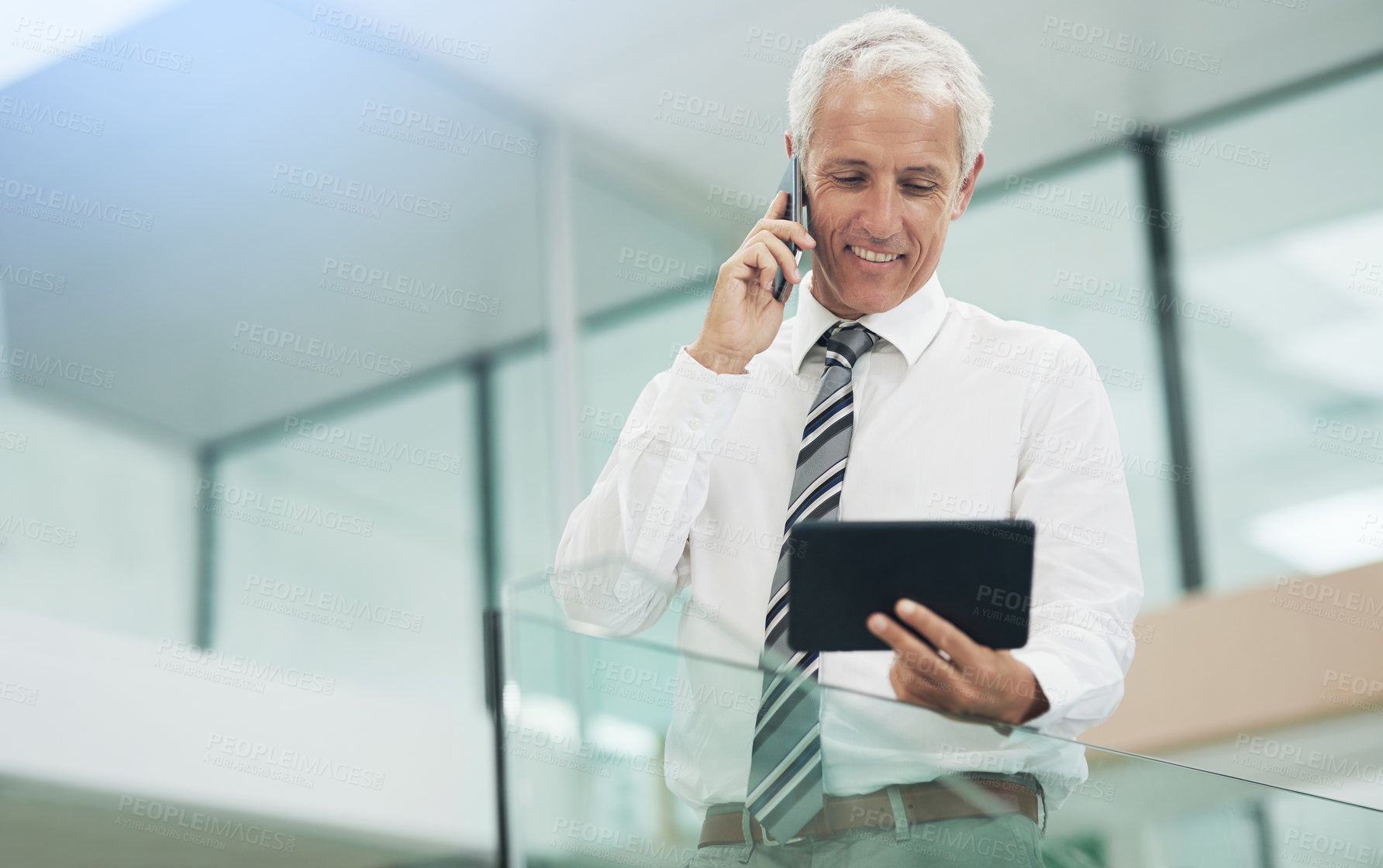 Buy stock photo Cropped shot of a businessman using a tablet while talking on his cellphone in the office