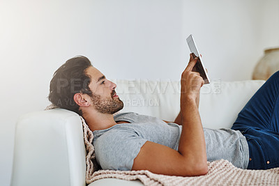 Buy stock photo Shot of a young man browsing the internet at home on a digital tablet