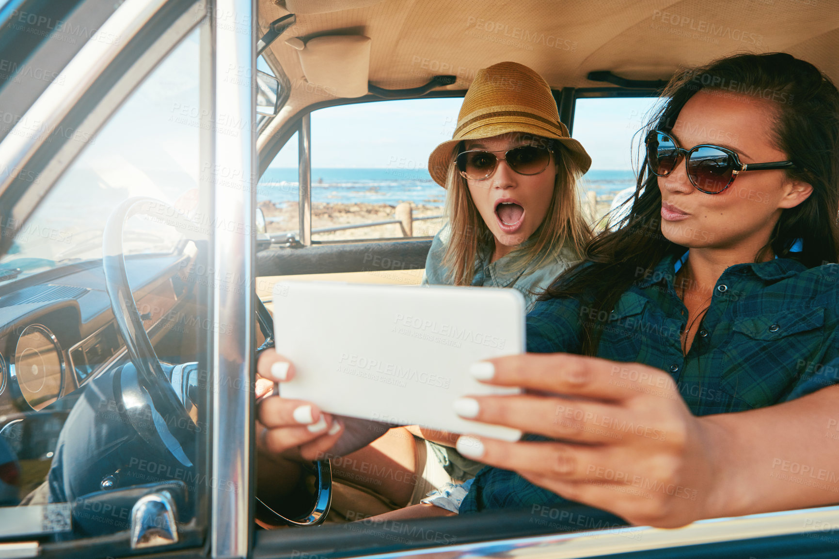 Buy stock photo Shot of two friends taking a selfie while on a road trip near the ocean