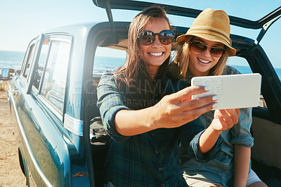 Buy stock photo Shot of two friends taking a selfie while on a road trip near the ocean
