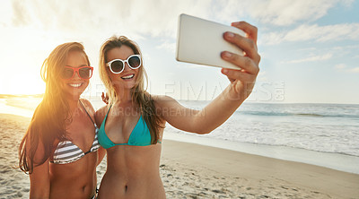 Buy stock photo Shot of two friends taking selfies while hanging out at the beach