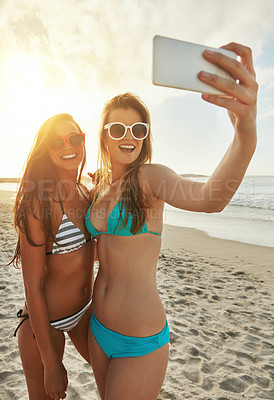 Buy stock photo Shot of two friends taking selfies while hanging out at the beach