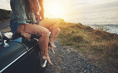 Buy stock photo Cropped shot of two friends sitting on the hood of a car while on a road trip