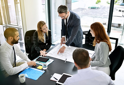 Buy stock photo Shot of a team of architects going over a blueprint during a formal meeting in an office