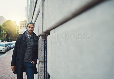 Buy stock photo Cropped shot of a fashionable young man leaning against a building in an urban setting