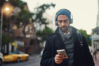 Buy stock photo Cropped shot of a fashionable young man listening to music on his phone while out in the city