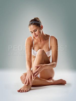 Buy stock photo Studio shot of a young woman in underwear caressing her legs against a gray backgroundt